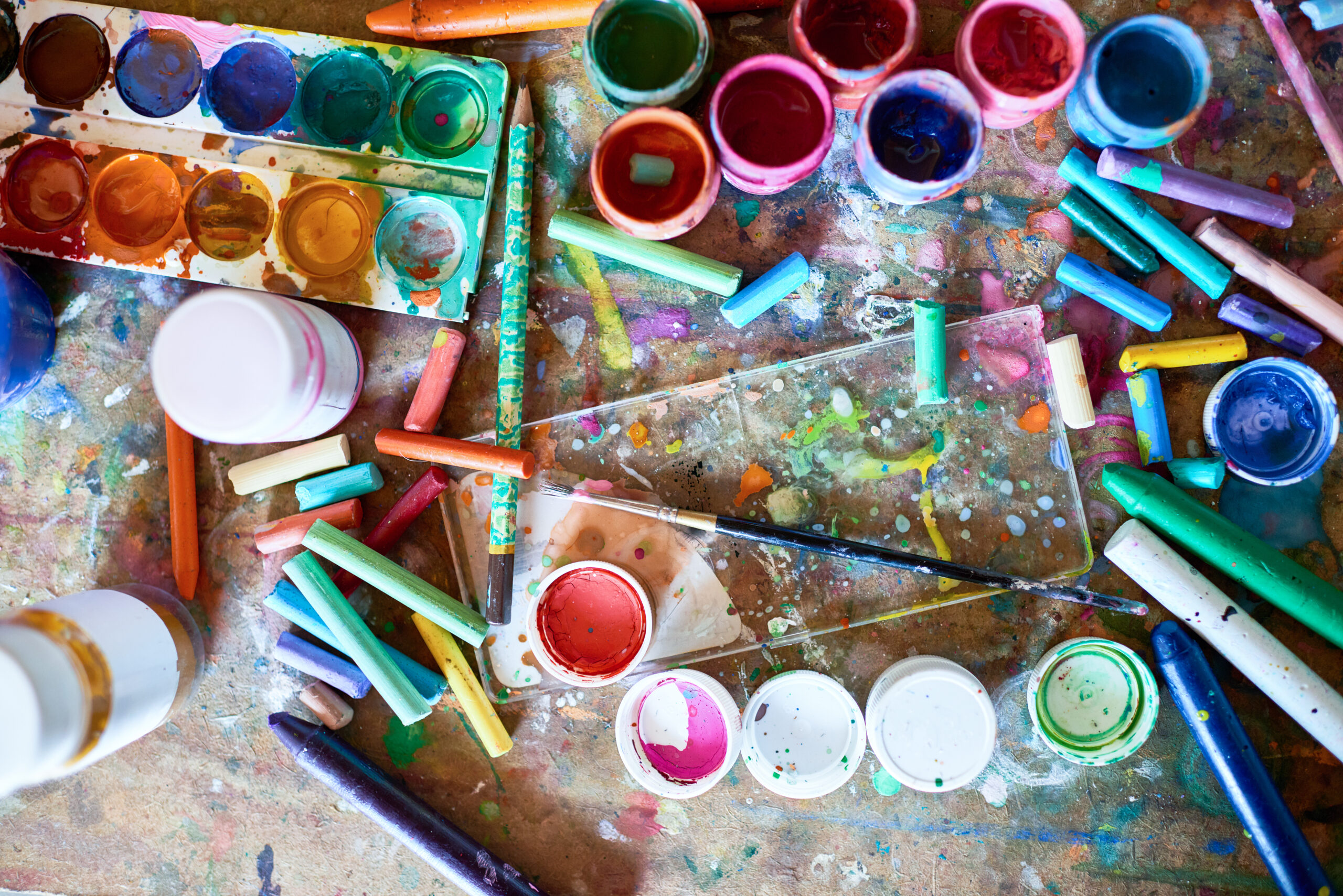 Background image of painting supplies on shabby wooden table: paintbrushes, pastels and watercolors splashed with paints