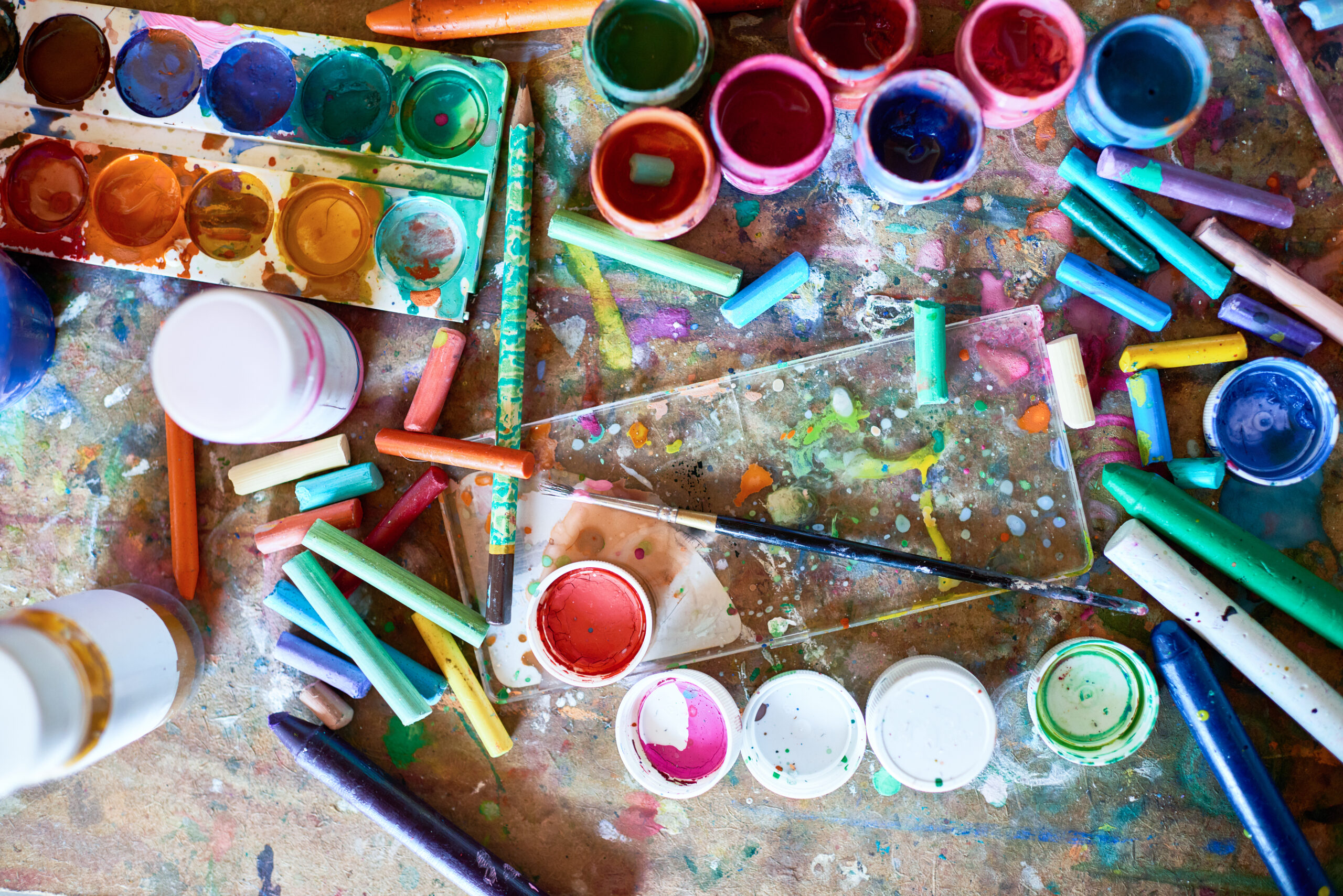 Background image of painting supplies on shabby wooden table: paintbrushes, pastels and watercolors splashed with paints